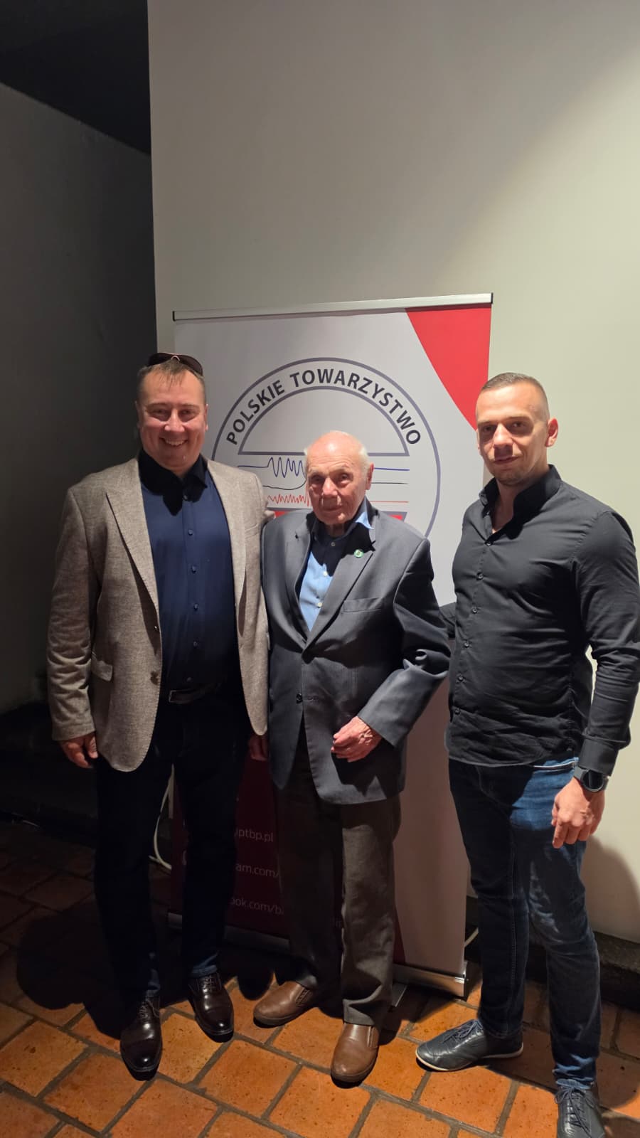 Dr Marcin Gołaszewski, płk dr inż. Łucjan Wiśniewski i Jakub Bartnicki przy banerze PTBP na seminarium w Reszlu